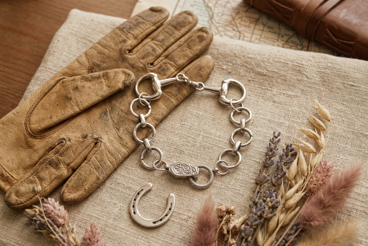 A silver-tone metal bracelet featuring a combination of thick and thin circular links, a horsebit clasp, and a decorative oval charm, displayed on a neutral gray background.