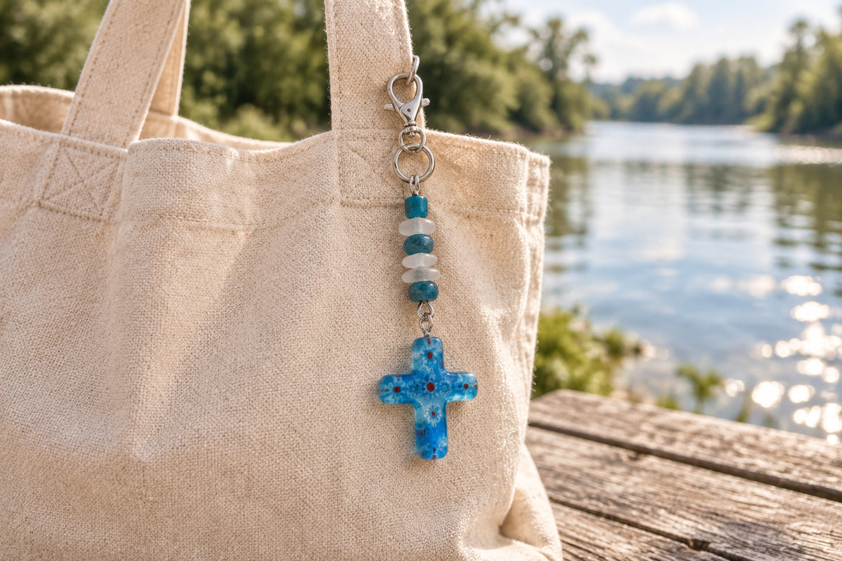 A small blue glass cross keychain with silver metal rings and a lobster clasp, shown on a plain light gray background.
