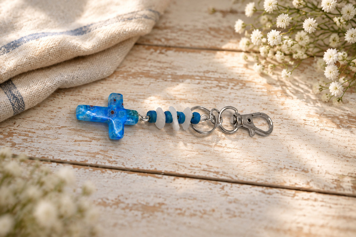 A small blue glass cross keychain with silver metal key rings and a lobster clasp, shown on a plain light gray background.