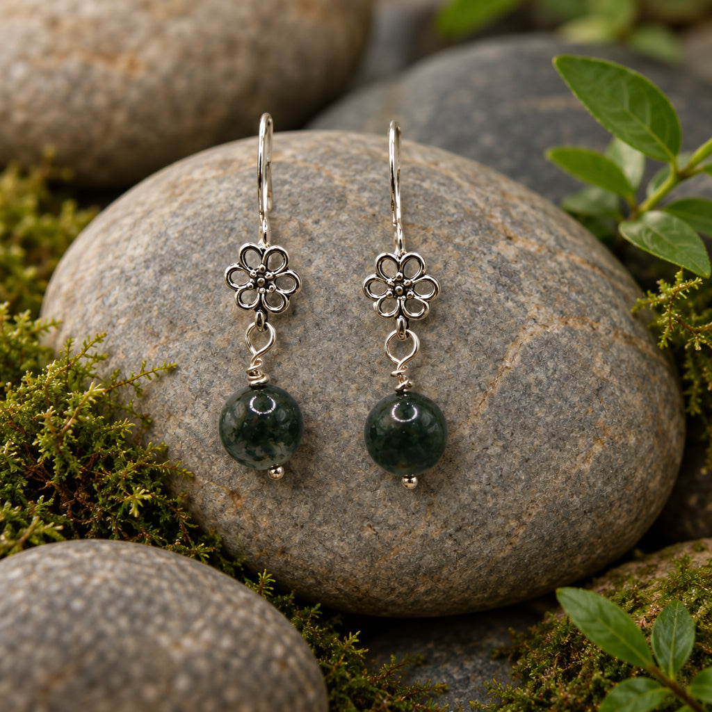 A pair of dangling earrings with silver-toned metal flower-shaped charms and dark round beads, displayed on a clear acrylic stand against a light gray background.