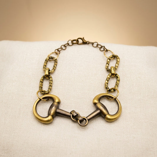 A horse bit chain bracelet featuring gold and silver-tone metal links, displayed on a plain light gray background.