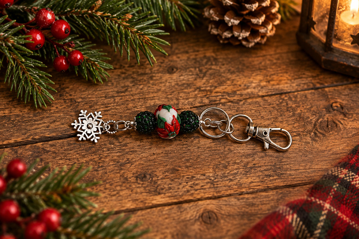 A silver-tone metal keychain charm featuring a snowflake charm, a red, green, and white beaded accent, and a lobster clasp, shown on a plain gray background.
