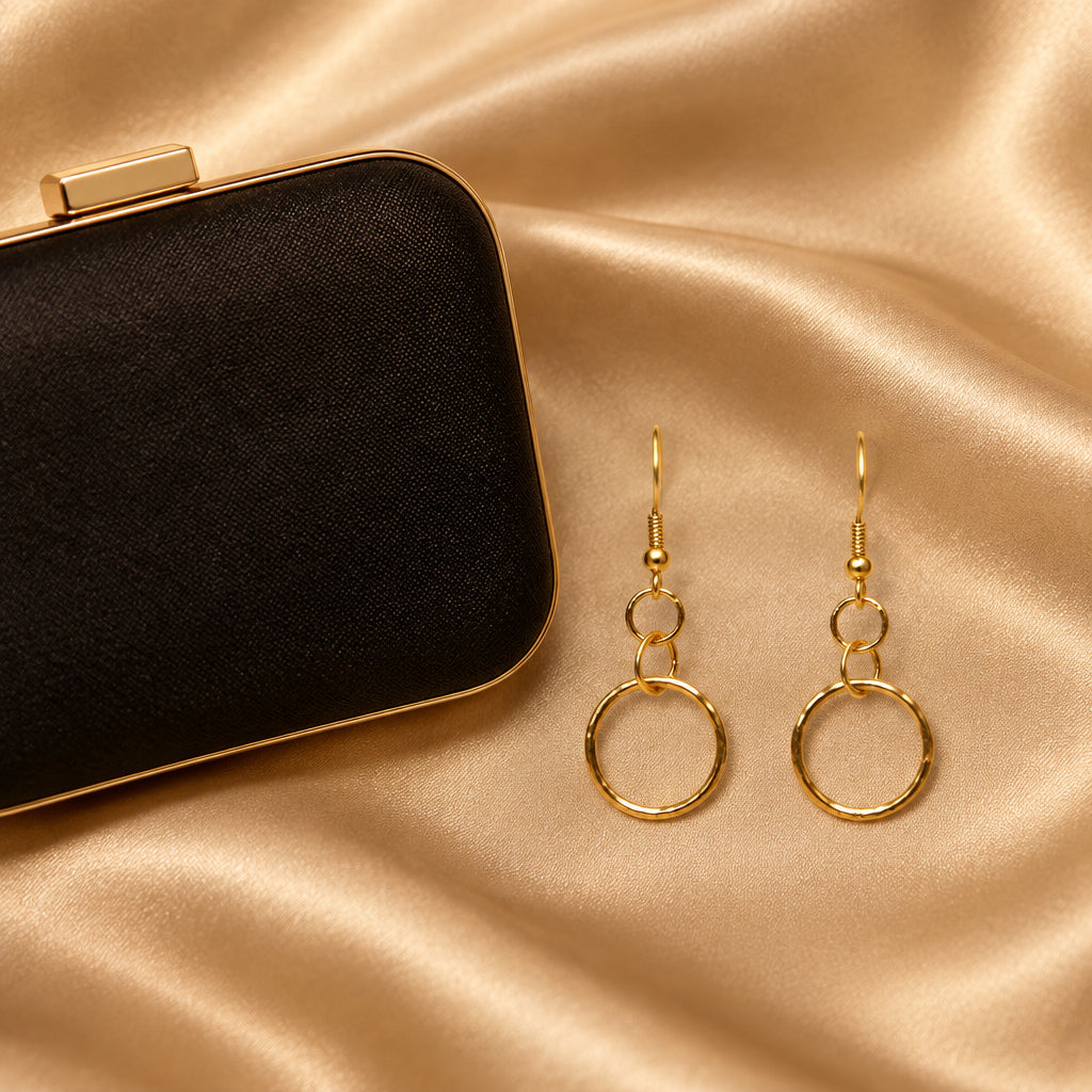 A pair of gold-toned drop earrings with open circular rings, displayed on a clear acrylic stand against a light gray background.