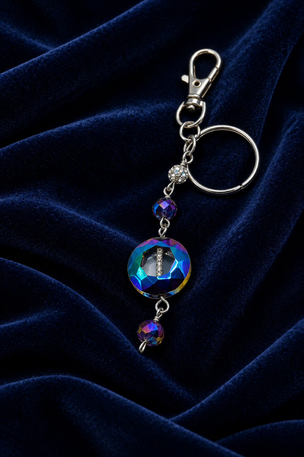 A silver metal keychain charm featuring a large round iridescent blue-green bead and two smaller dangling beads, shown on a plain light gray background.