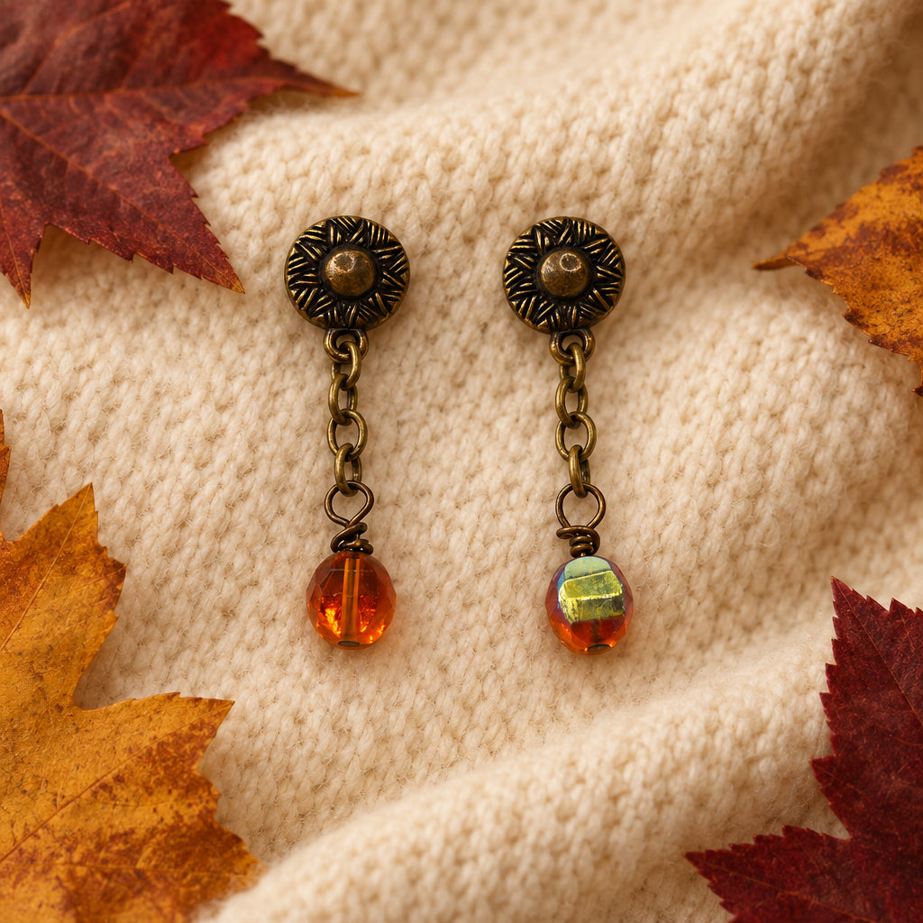 A pair of antique bronze dangle earrings with amber glass beads, displayed on a white 'River Inspired' jewelry card.