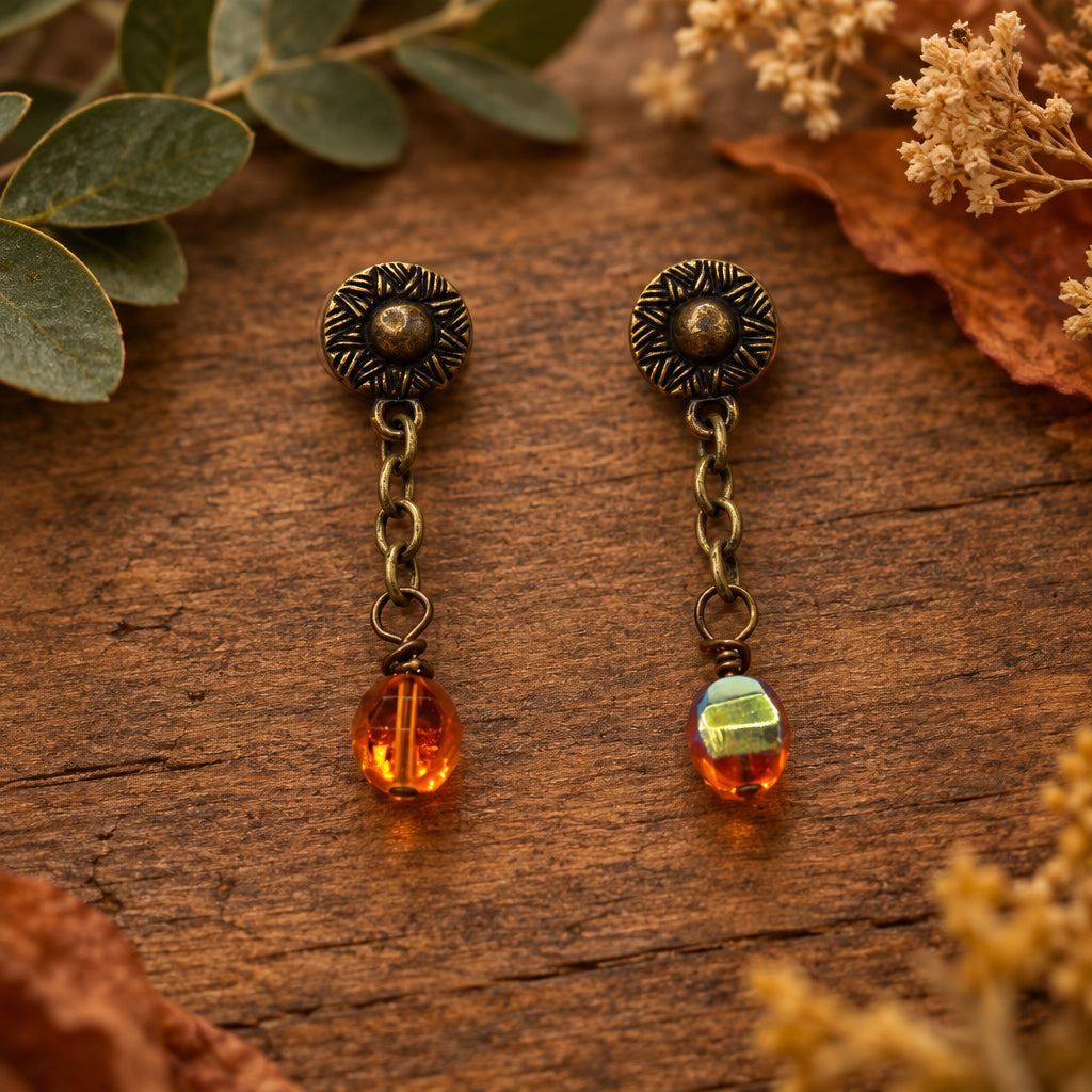 A pair of antique bronze dangle earrings with amber-orange beads, displayed on a white 'River Inspired' jewelry card.