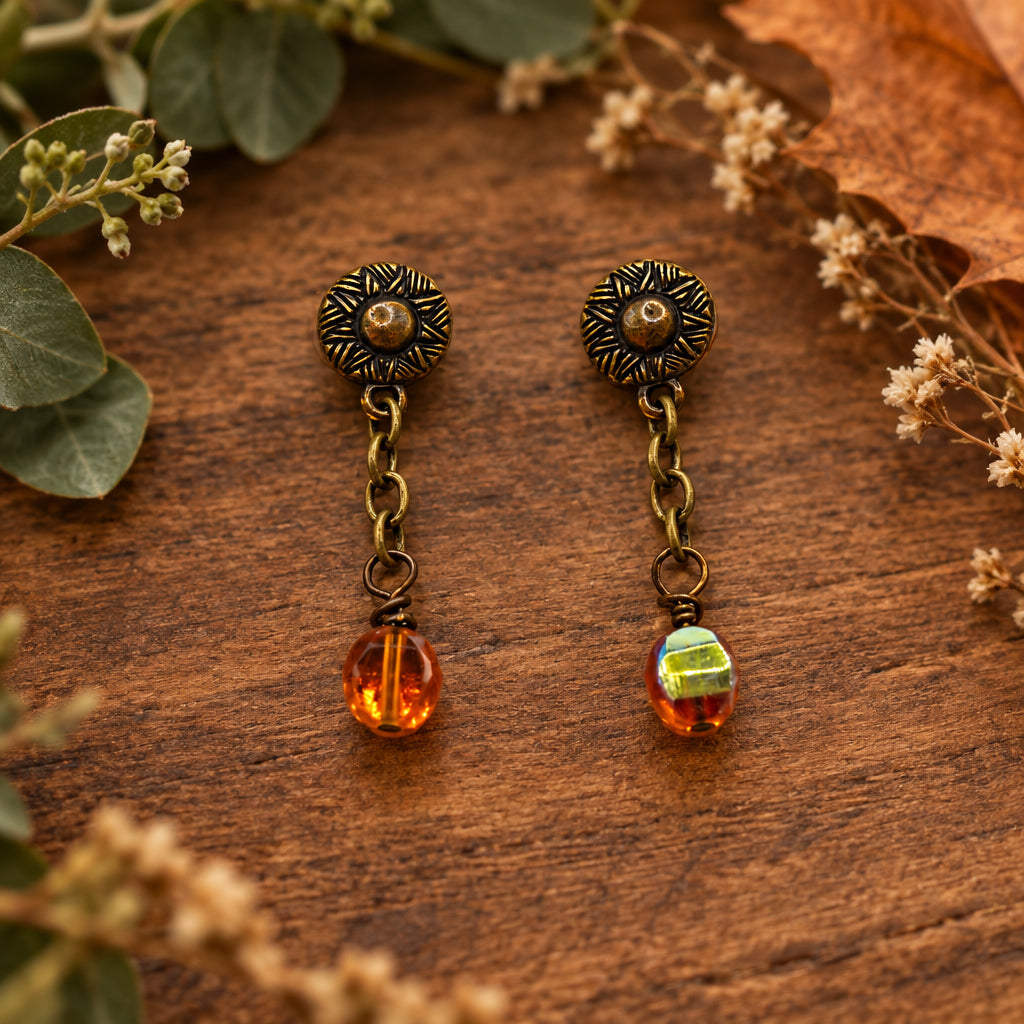 A pair of antique bronze dangle earrings with amber glass beads, displayed on a white card labeled 'River Inspired Handcrafted Jewelry'.