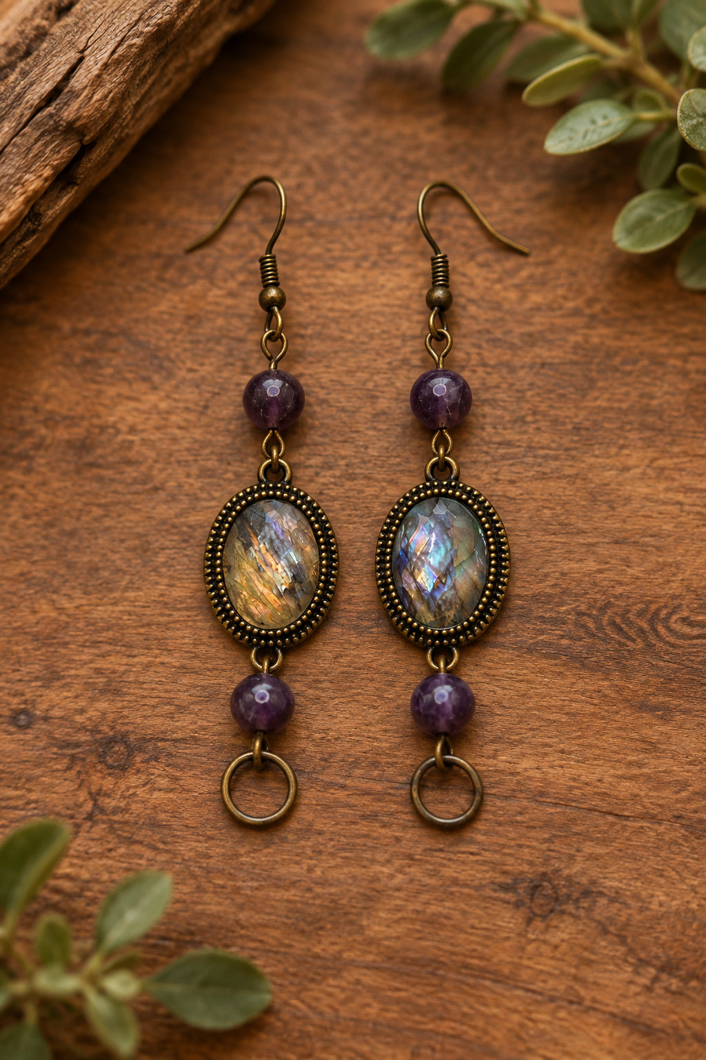 A pair of dangling earrings displayed on a white card labeled River Inspired Handcrafted Jewelry. The earrings have antique bronze-toned metal frames with iridescent abalone shell centers and purple beads.