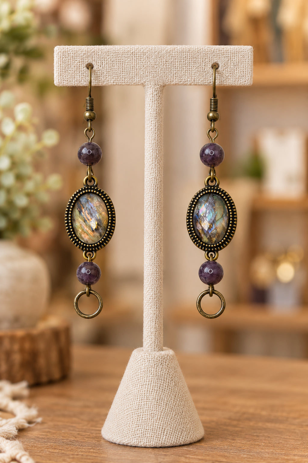 A pair of handmade dangle earrings displayed on a white card. Each earring has an oval iridescent abalone shell centerpiece in an antique bronze frame, flanked by purple beads and hanging from antique bronze fishhook wires.