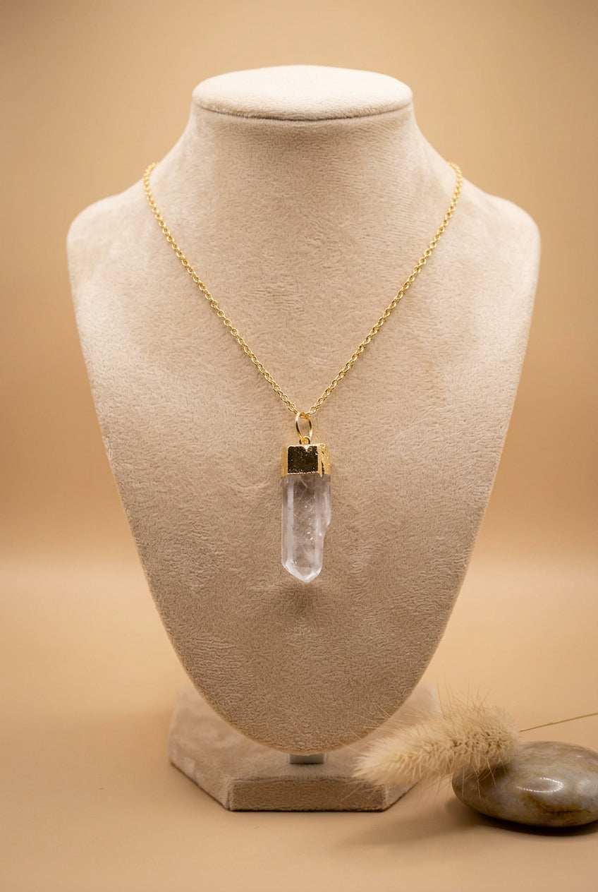 A gold chain necklace with a clear quartz crystal pendant, displayed on a black velvet jewelry bust with a hand holding the left side.