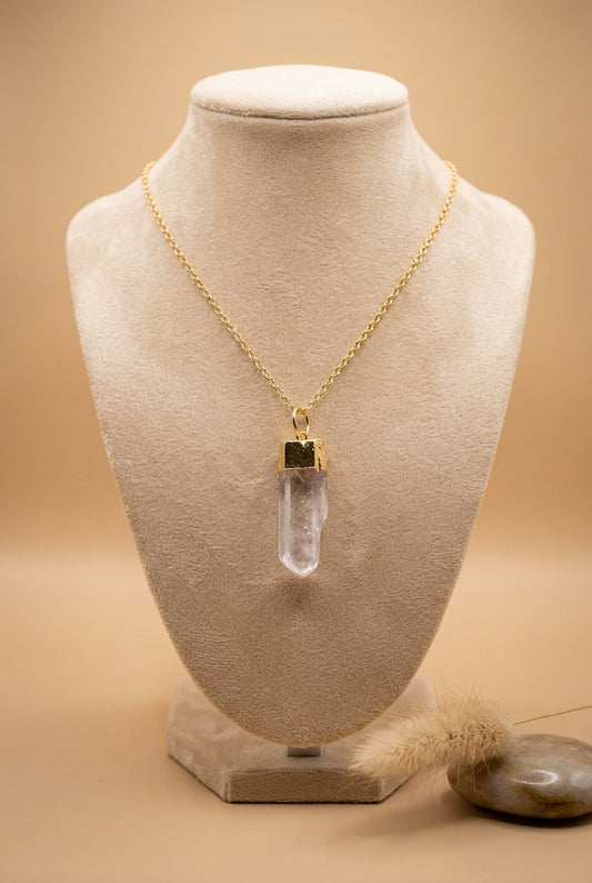 A gold chain necklace with a clear quartz crystal pendant, displayed on a black velvet jewelry bust with a hand holding the left side.