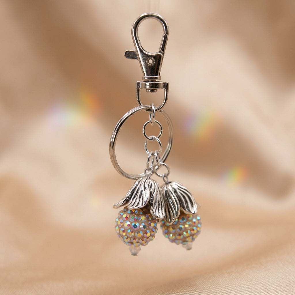 A silver metal keychain featuring two dangling acorn-shaped charms covered in iridescent rhinestones, attached to a split key ring and lobster clasp, shown on a plain light gray background.