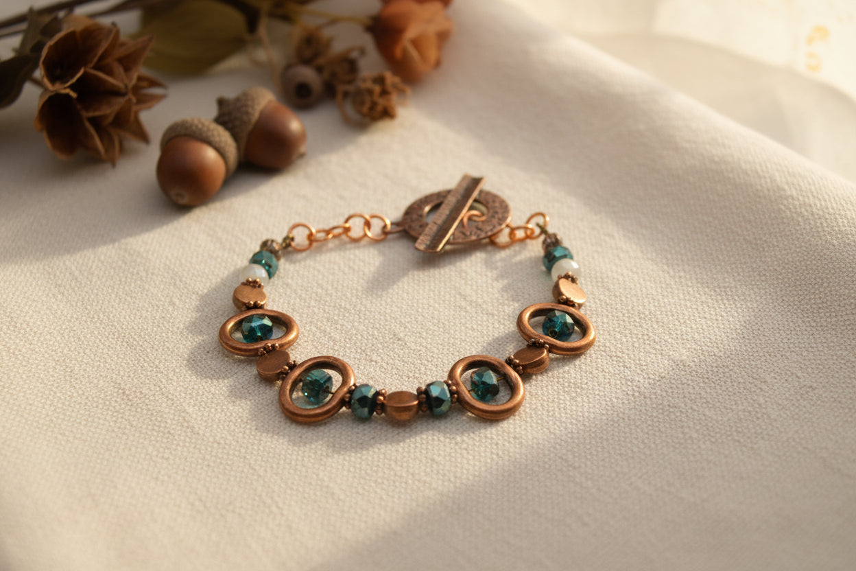A handmade beaded bracelet with copper-toned metal rings, faceted brown beads, and dark green iridescent beads, featuring a rustic copper toggle clasp, shown on a plain light gray background.