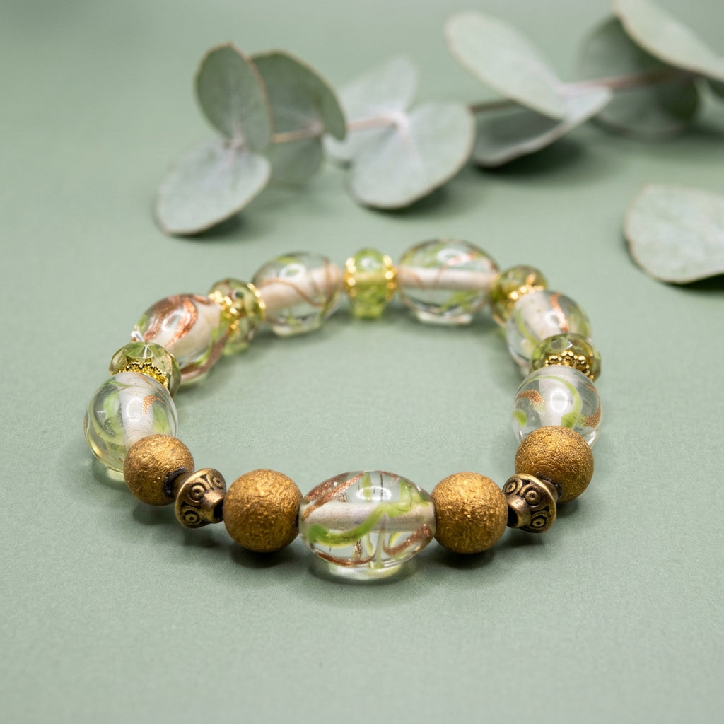 A beaded stretch bracelet featuring gold-toned matte beads, clear glass beads with white and green swirls, and small metallic gold spacers, displayed on a plain light gray background.