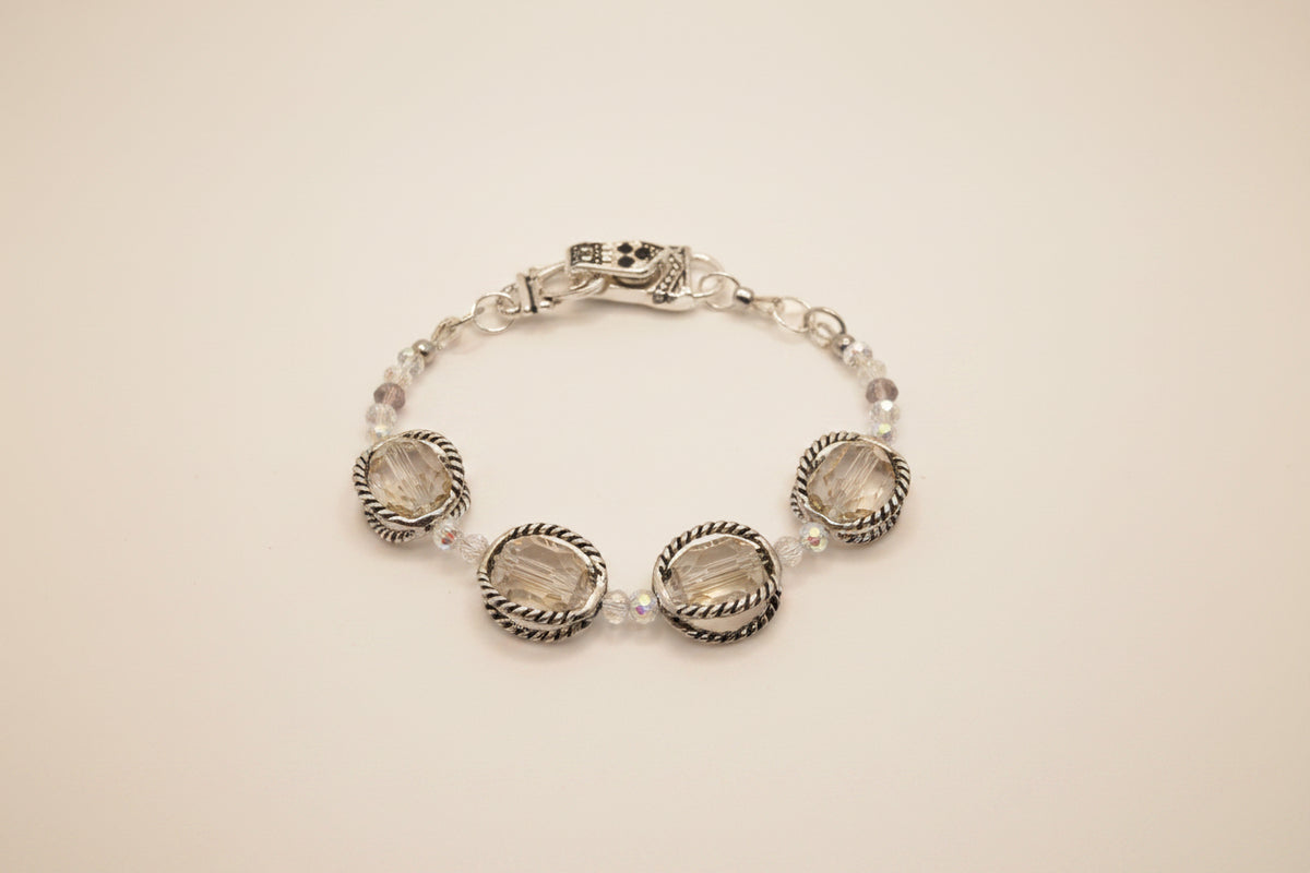 A silver-toned beaded bracelet with three large oval clear faceted gemstones and smaller clear beads, displayed on a neutral light gray background.