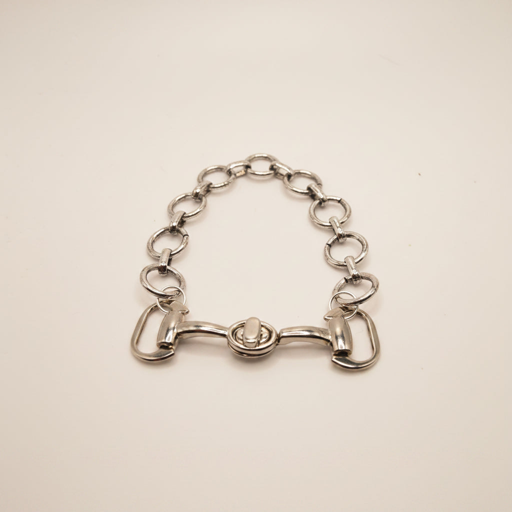 A silver horse bit chain bracelet with a central horsebit clasp, displayed on a neutral gray background.