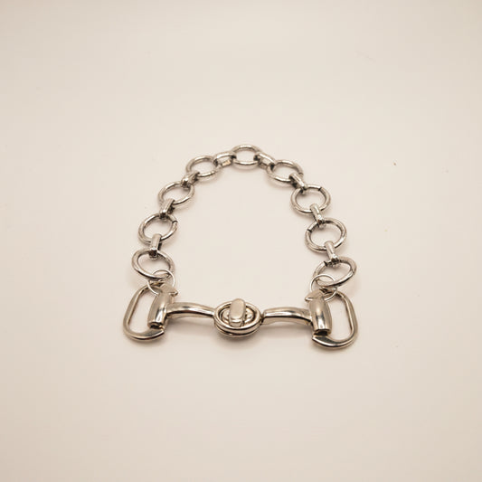 A silver horse bit chain bracelet with a central horsebit clasp, displayed on a neutral gray background.
