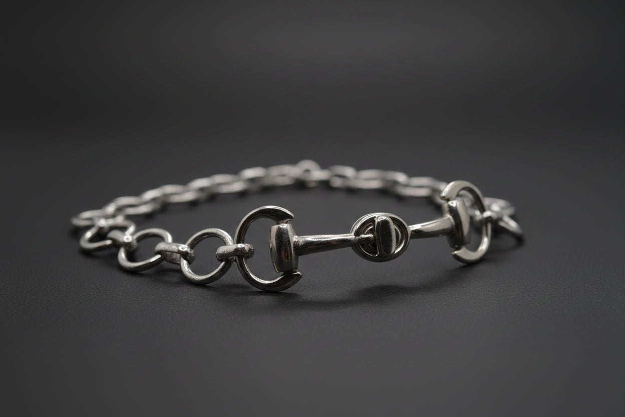 A silver horse bit chain bracelet with interlocking rings and a central horse bit clasp, displayed on a neutral light gray background.