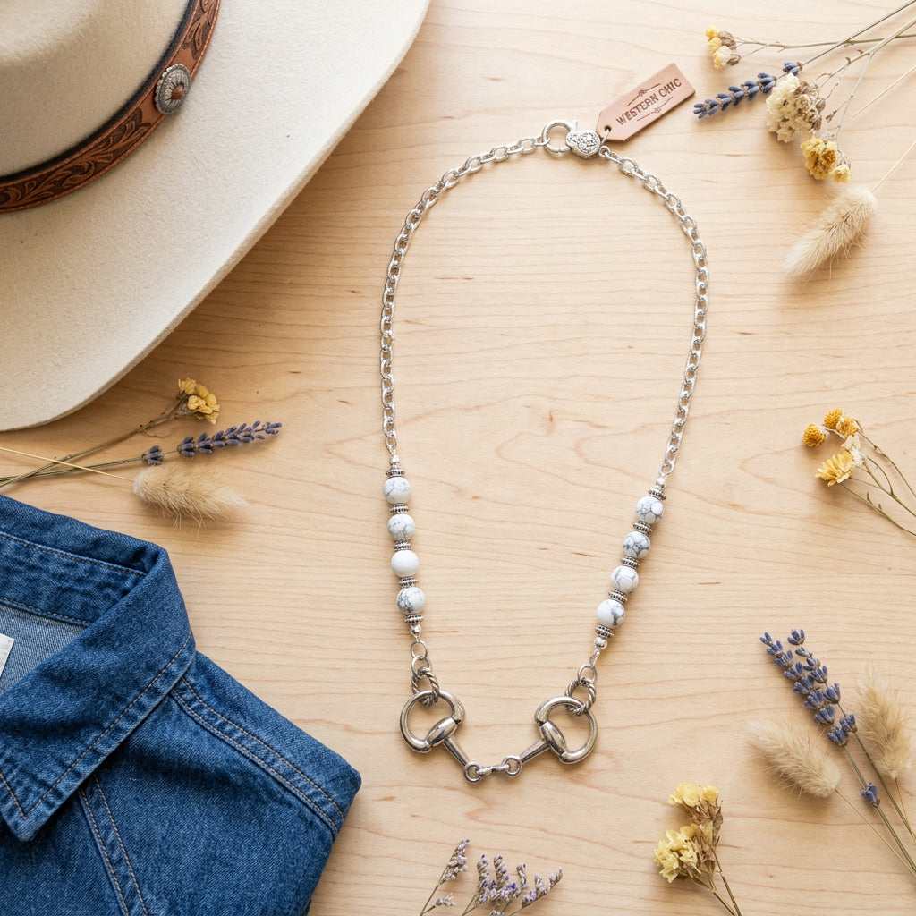 A silver-toned beaded necklace with a horsebit clasp and a small lobster clasp extension, displayed on a white background.