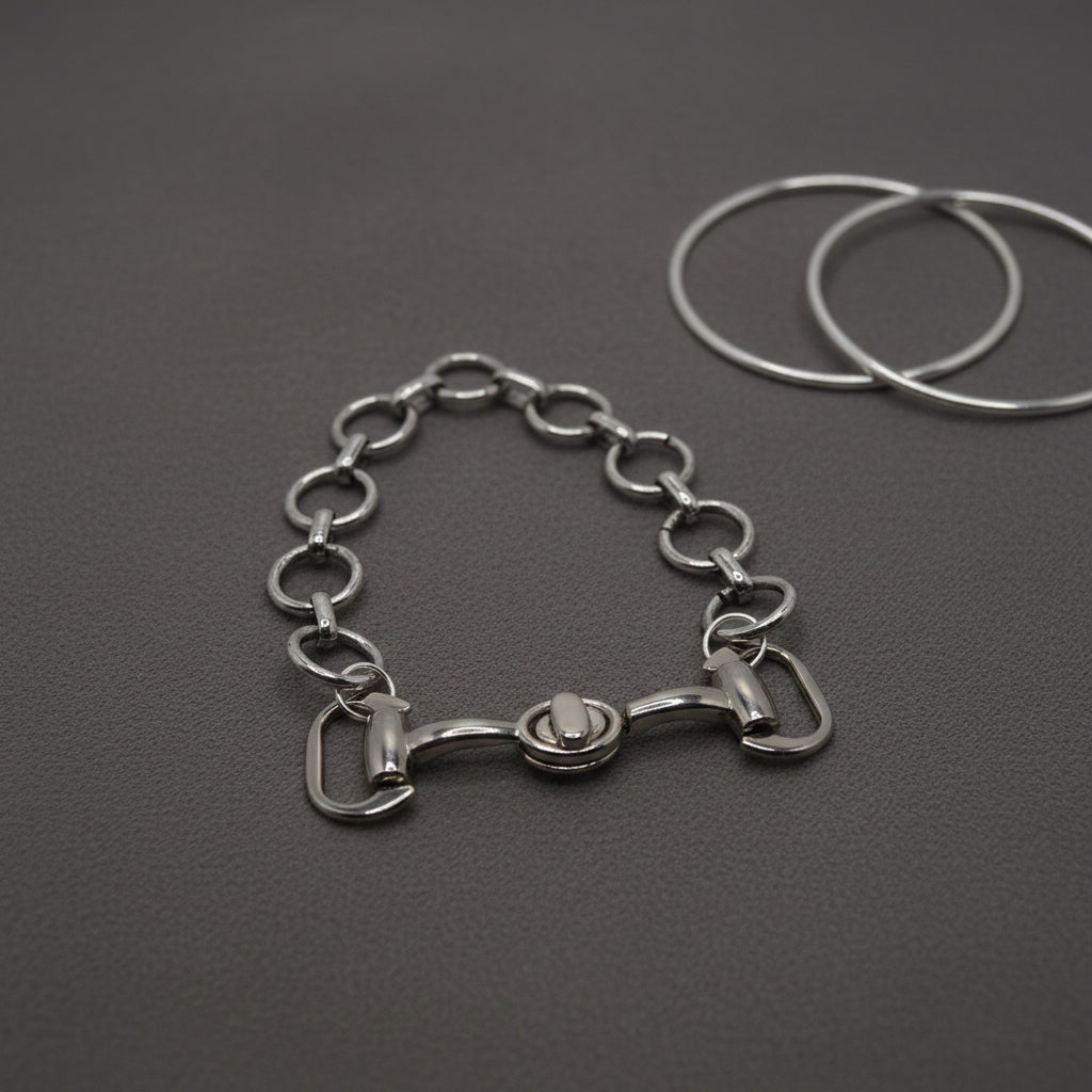 A silver-toned metal chain bracelet featuring a horse bit motif at the center, displayed on a plain light gray background.