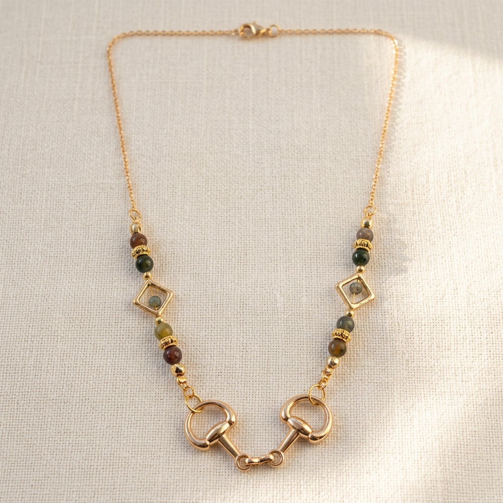 A gold-toned necklace featuring horsebit charms and dark green beads, displayed on a light gray surface.