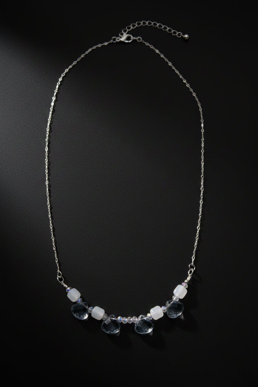 A delicate silver chain necklace featuring a row of faceted light blue beads and small clear beads, displayed against a plain light gray background.