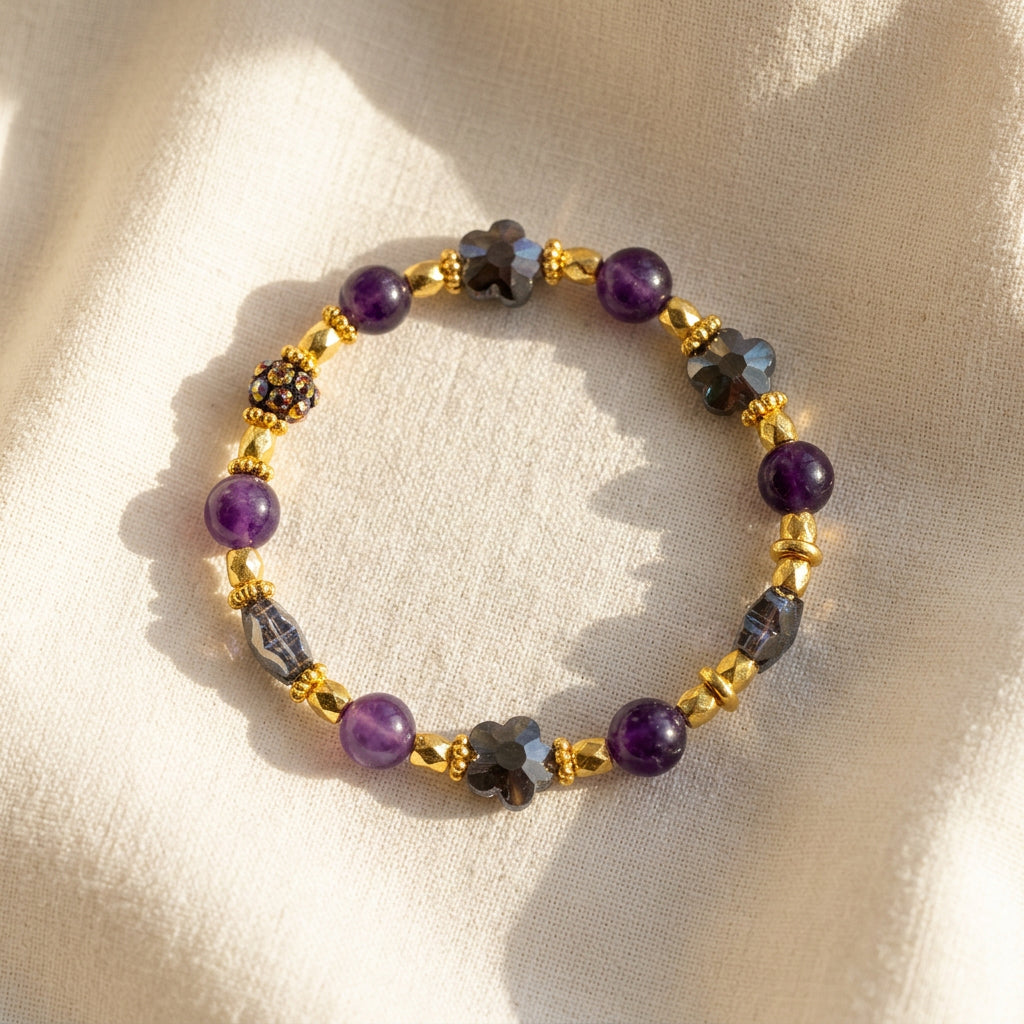 A beaded stretch bracelet featuring purple round beads, gray faceted beads, and shiny gold spacer beads, arranged in a circle on a plain light gray background.