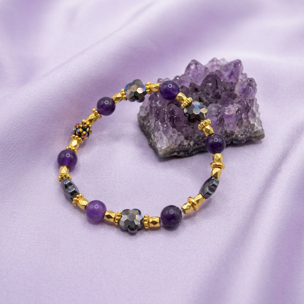 A beaded stretch bracelet featuring purple beads, gold-toned spacer beads, and gray elephant-shaped beads, displayed on a plain light gray surface.