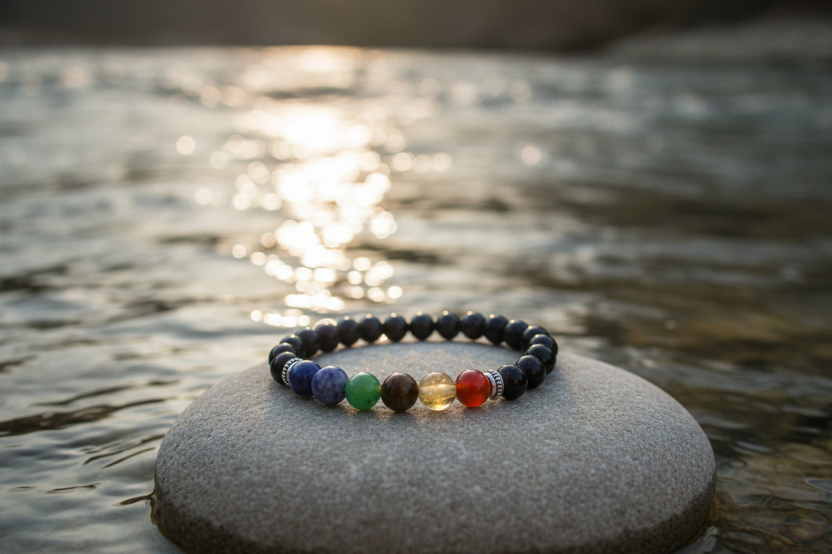 A beaded chakra bracelet made of black round beads with seven colorful accent beads representing the chakras, displayed on a light gray background.