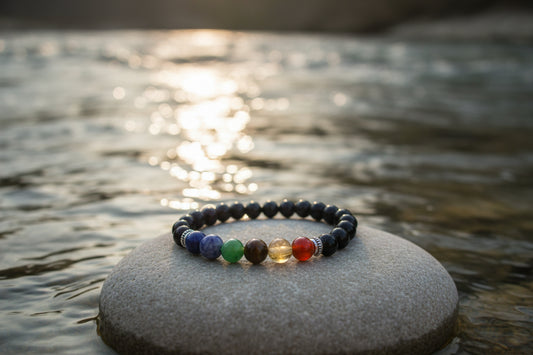 A beaded chakra bracelet made of black round beads with seven colorful accent beads representing the chakras, displayed on a light gray background.