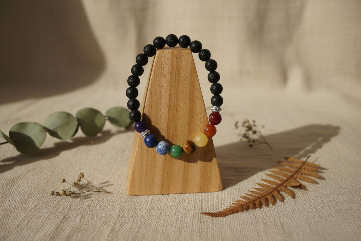 A beaded chakra bracelet made of black round beads with seven colorful accent beads representing the chakras, displayed on a light gray background.