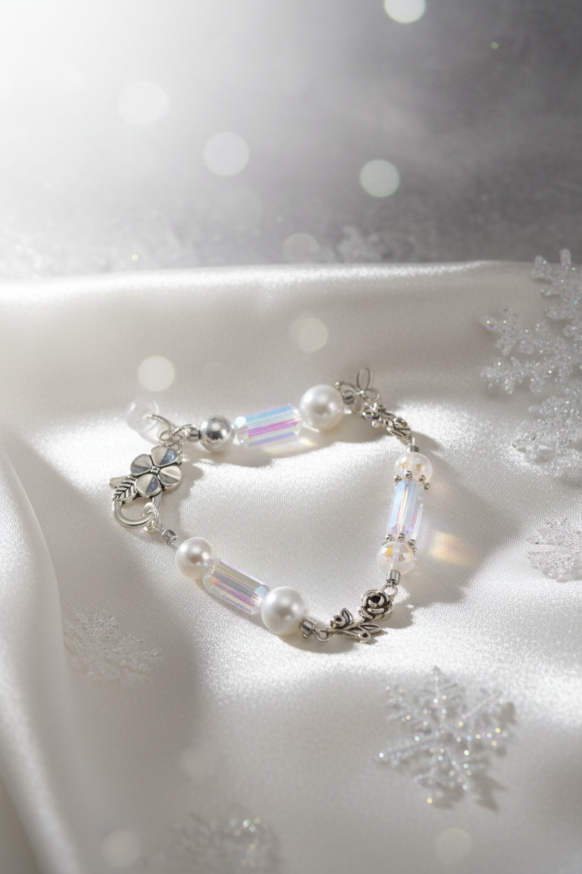 A silver-toned beaded bracelet featuring white faux pearls, iridescent rectangular beads, and a silver-toned floral clasp, displayed on a plain gray background.