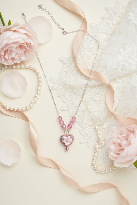 A pink beaded necklace with a glittery heart-shaped pendant, displayed on a black velvet jewelry bust against a white background.