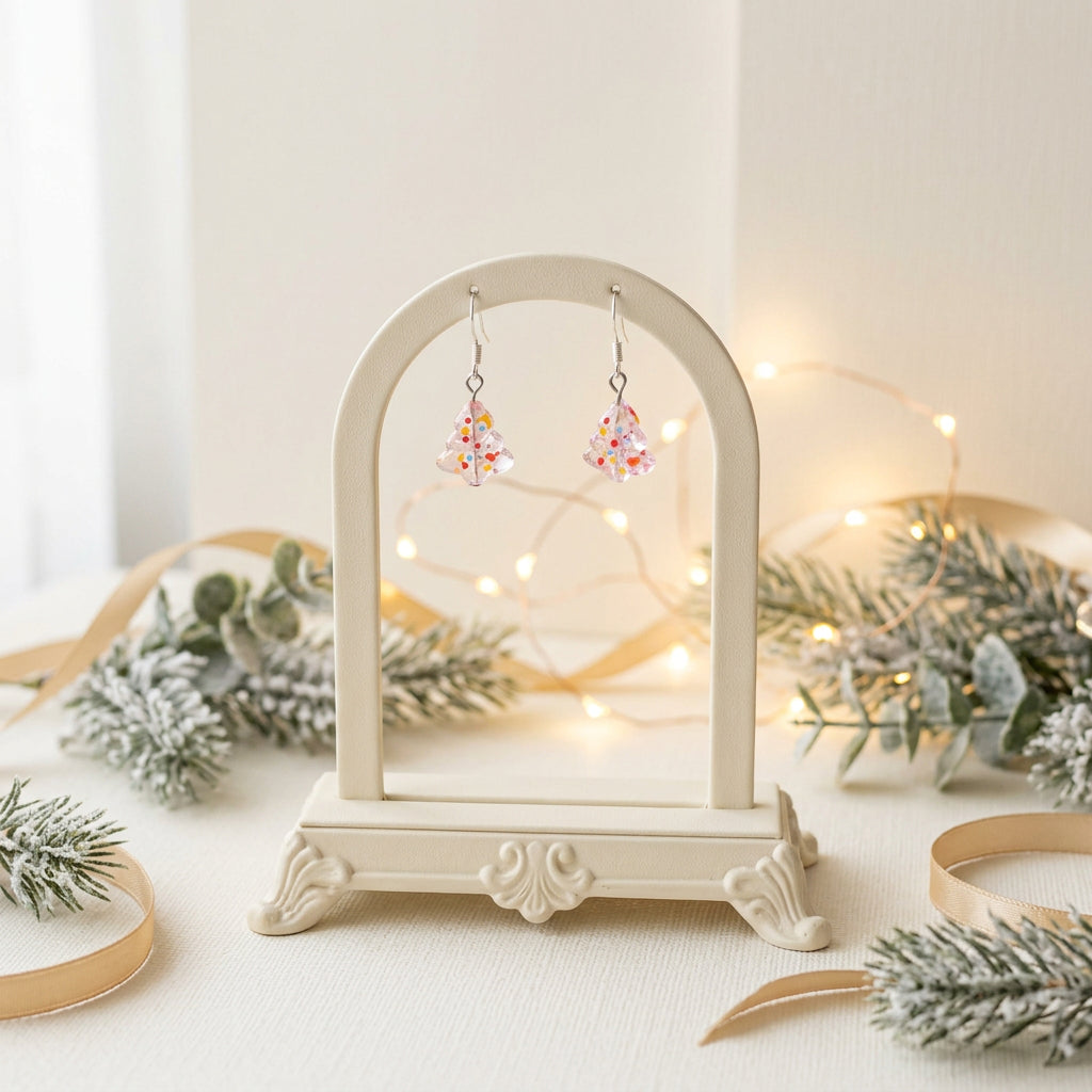 A pair of small dangling earrings displayed on a clear acrylic stand against a plain light gray background. The earrings appear to be silver-toned hooks with translucent or clear bell- or flower-like charms containing small multicolored speckles.
