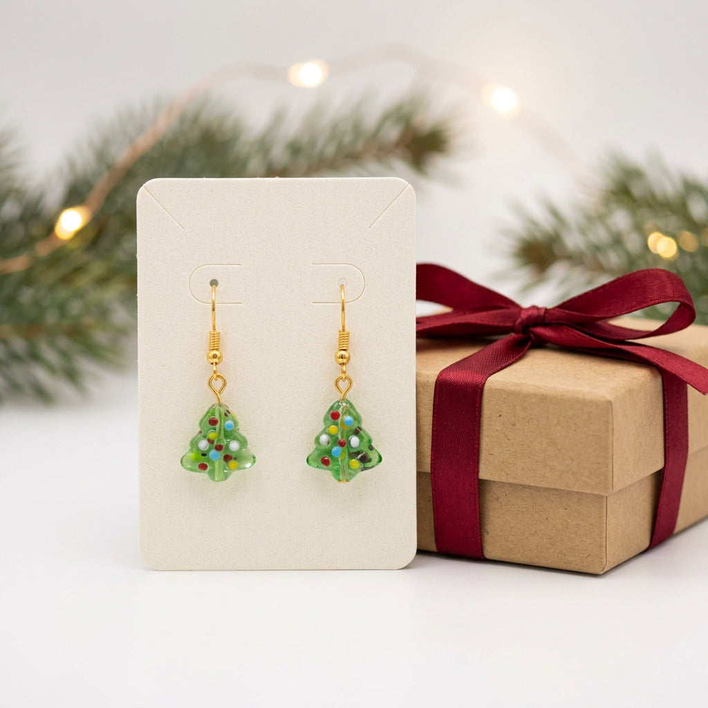 A pair of gold-tone dangle earrings with green, marbled, textured tree-shaped charms, displayed on a clear acrylic stand against a neutral gray background.