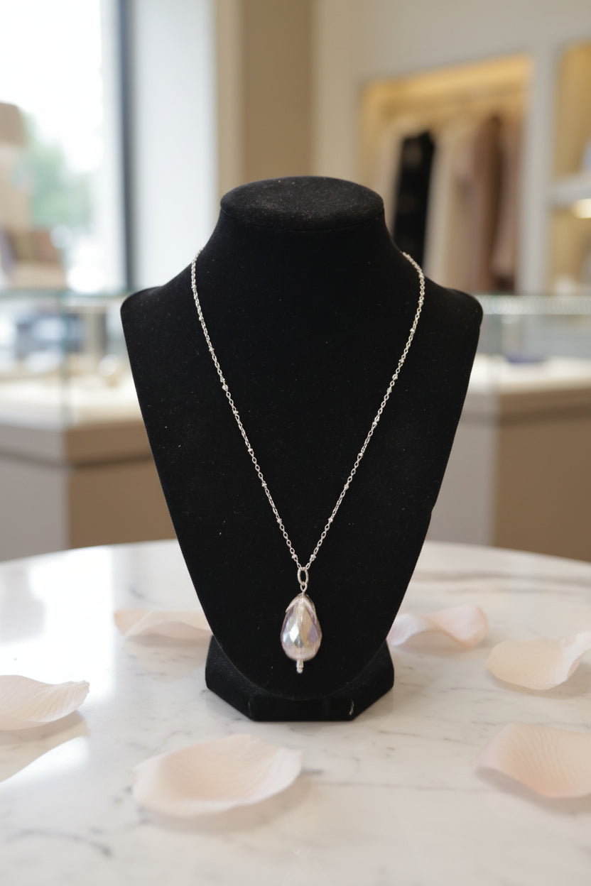 A silver chain necklace with a teardrop-shaped iridescent pendant displayed on a black velvet jewelry bust against a white background.