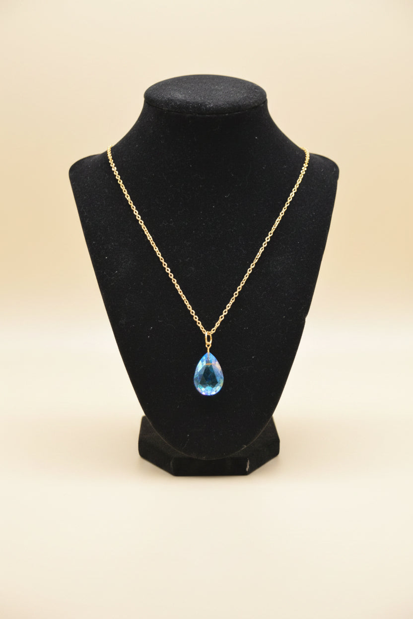 A gold chain necklace with a small teardrop-shaped blue and gold pendant, displayed on a black velvet jewelry bust against a white background.