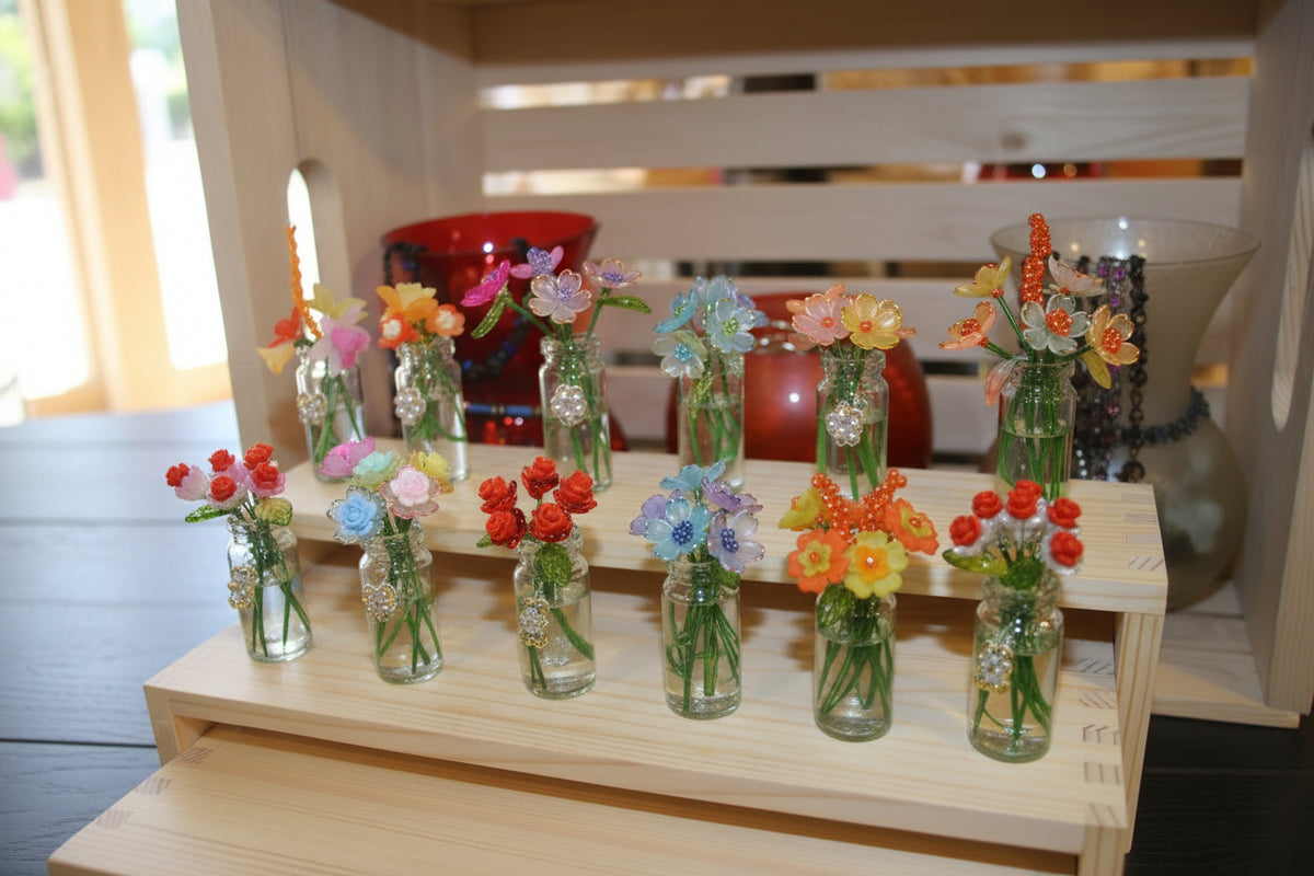 A wooden display stand holding multiple small clear glass vases filled with colorful artificial flowers, arranged on a dark wooden floor in front of a light wood shelving unit.