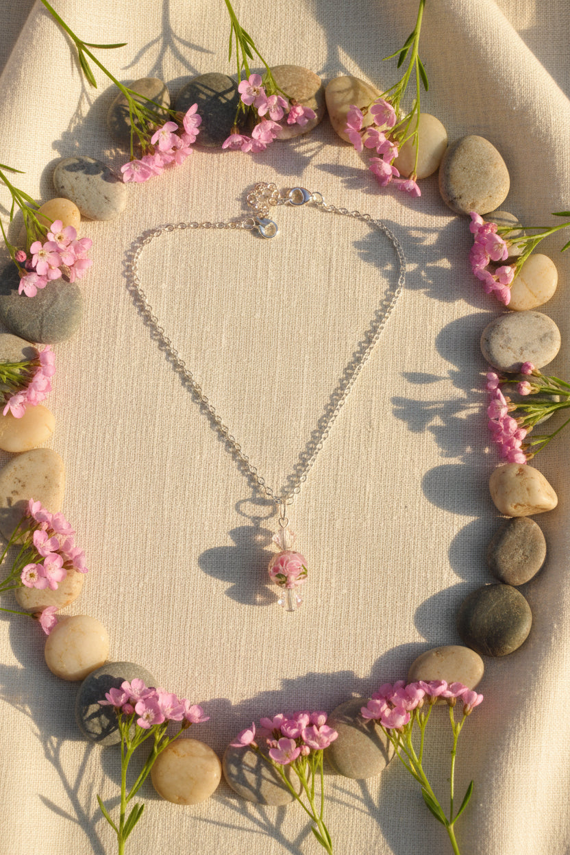 A silver chain necklace with a pendant featuring pink and iridescent beads, displayed on a black velvet necklace bust.