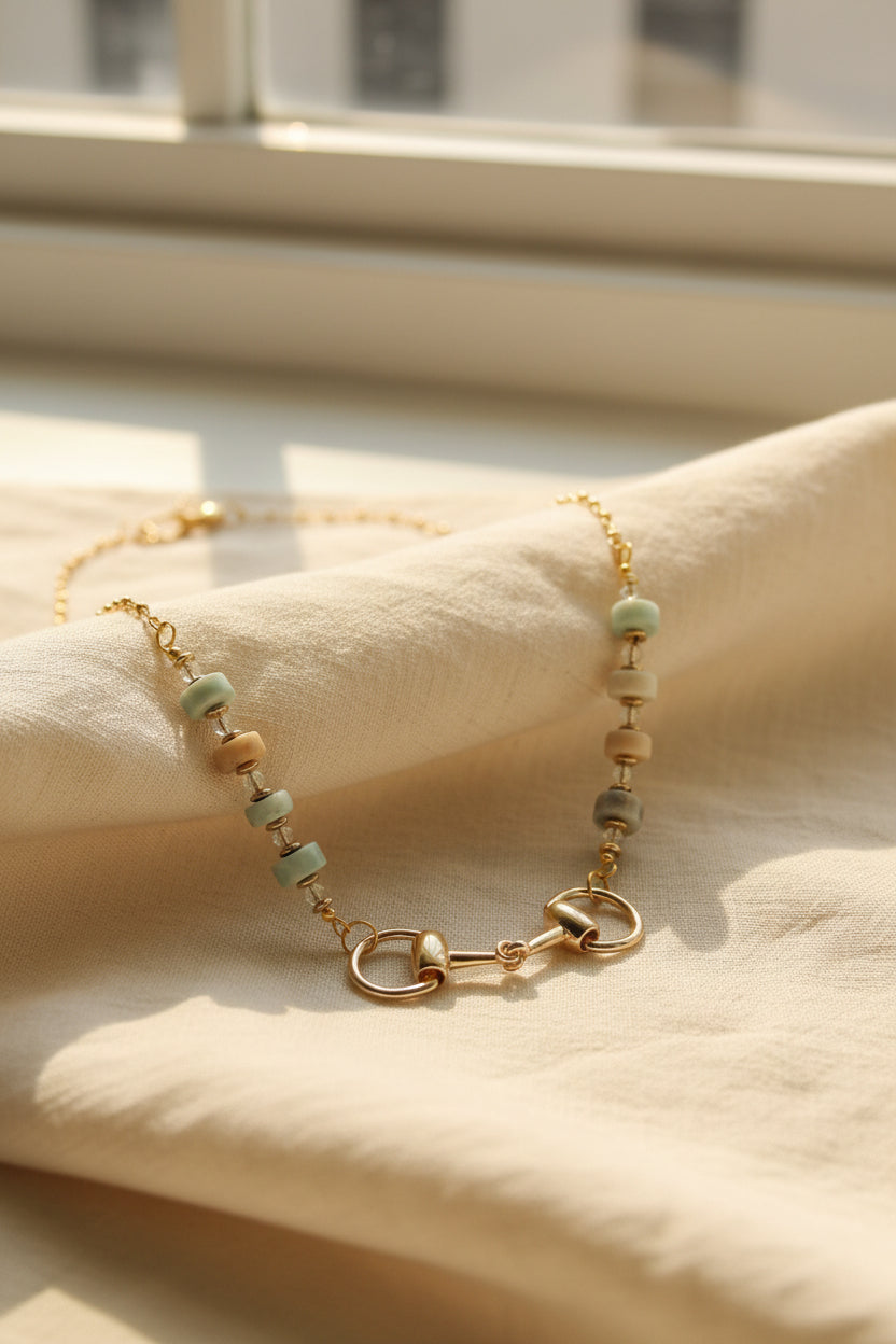 A gold-tone horse bit necklace with white and iridescent beads, displayed on a black velvet jewelry bust against a white background.