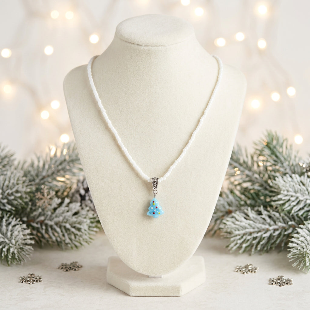 A silver-toned beaded necklace with a small turquoise Christmas tree pendant, displayed on a black velvet jewelry bust against a white background.