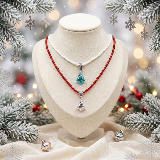 Two layered necklaces displayed on a black velvet jewelry bust against a white background. The top necklace is white with a small light blue Christmas tree pendant.