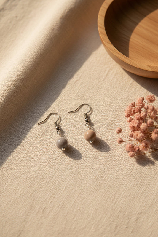 A pair of handmade dangle earrings with brown and gray marbled beads, displayed on a white card labeled 'River Inspired Handcrafted Jewelry' against a plain gray background.