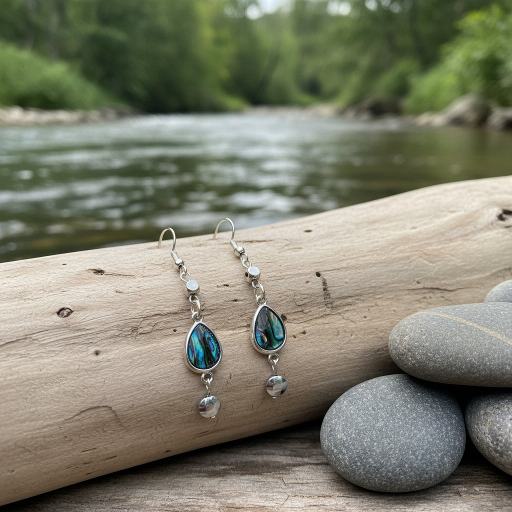 A pair of silver dangle earrings with iridescent teardrop-shaped stones and small silver beads, displayed on a clear stand against a light gray background.