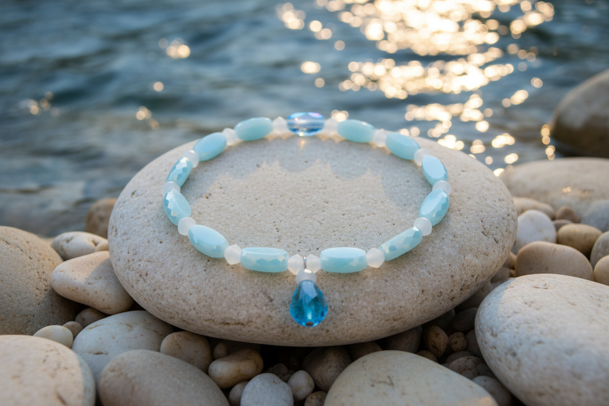 A beaded stretch bracelet featuring light blue and white beads, with one faceted light blue crystal charm hanging from the front, displayed on a neutral light gray background.