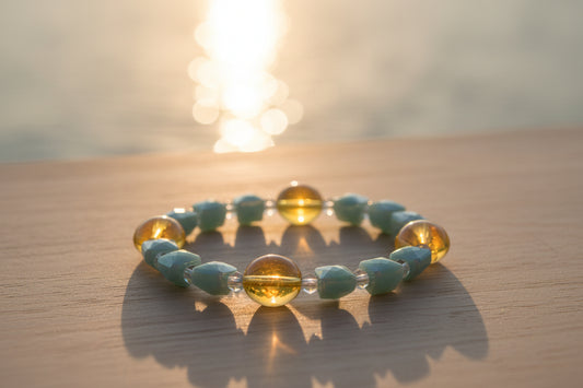A beaded stretch bracelet featuring faceted light blue beads and three larger round amber-yellow beads, displayed on a neutral light gray background.