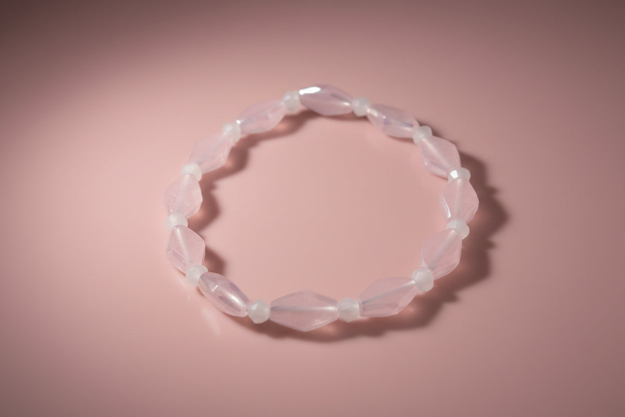 A beaded stretch bracelet featuring faceted light pink beads and small translucent white spacer beads, displayed on a plain light gray background.