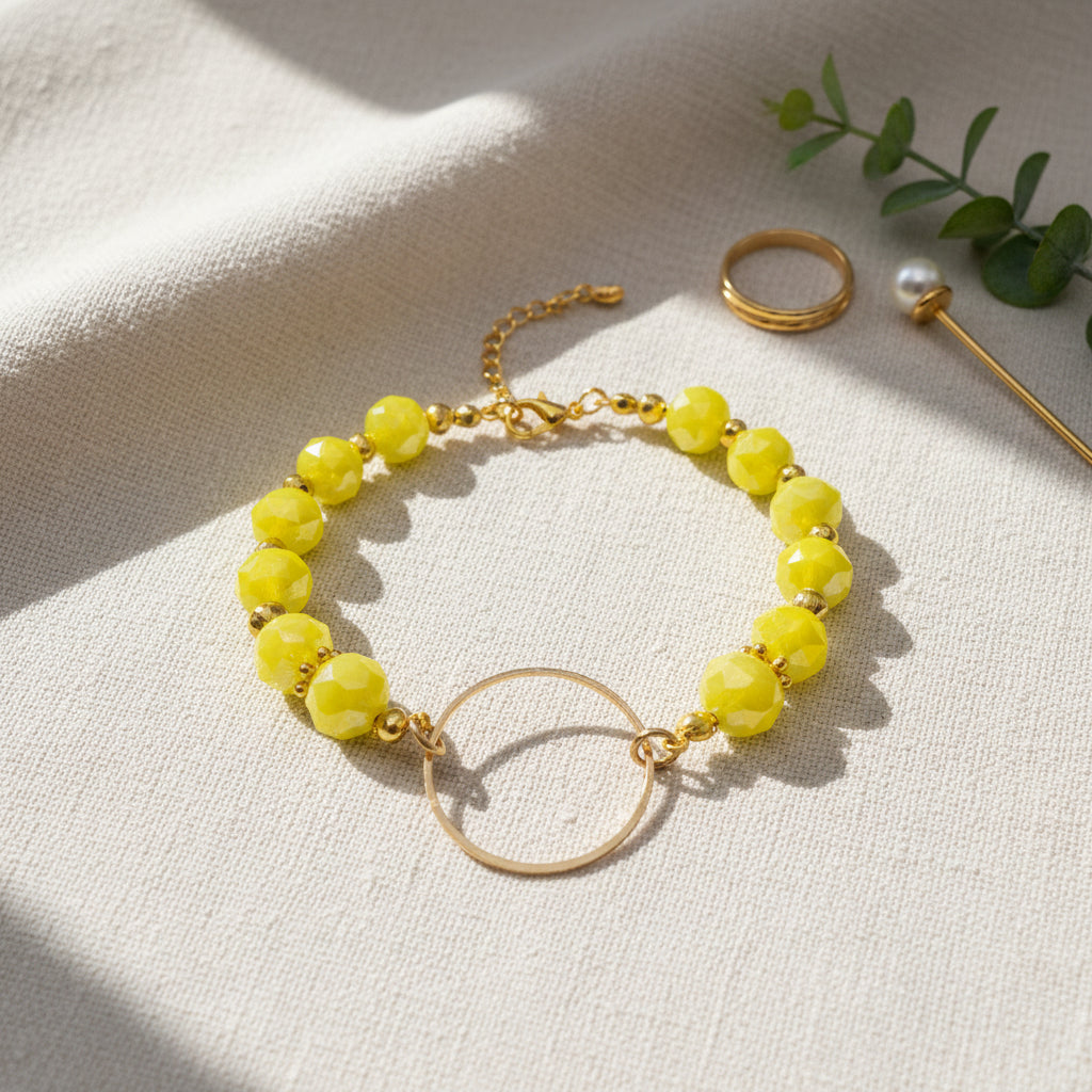 A gold-tone bracelet featuring faceted lime green beads and a large open circular gold-tone ring clasp, displayed on a neutral light gray background.