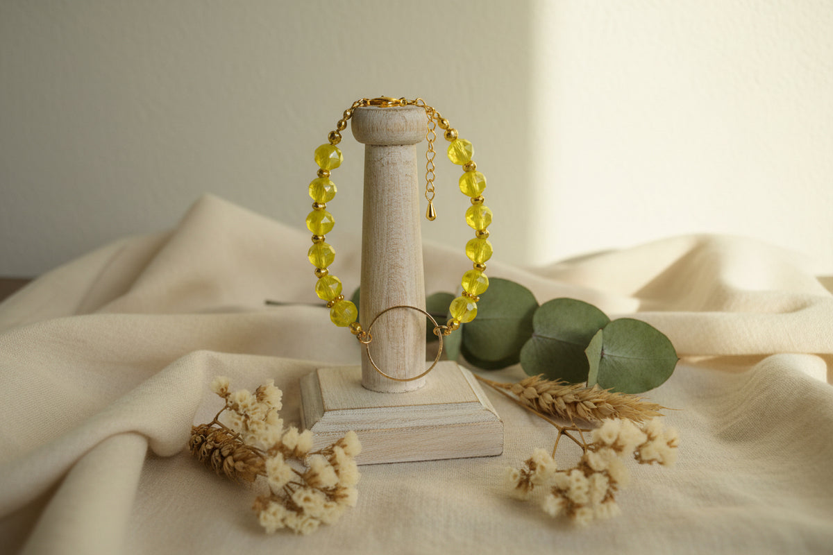 A gold-tone beaded bracelet featuring faceted yellow-green beads and a large textured gold-tone ring clasp, displayed on a neutral light gray background.