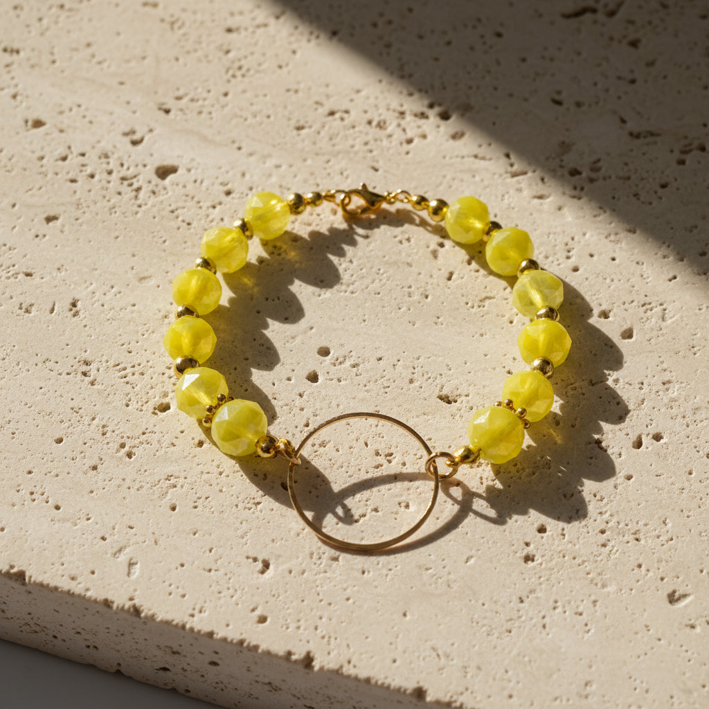 A yellow faceted bead bracelet with a gold-tone circular ring charm, displayed on a neutral light gray background.